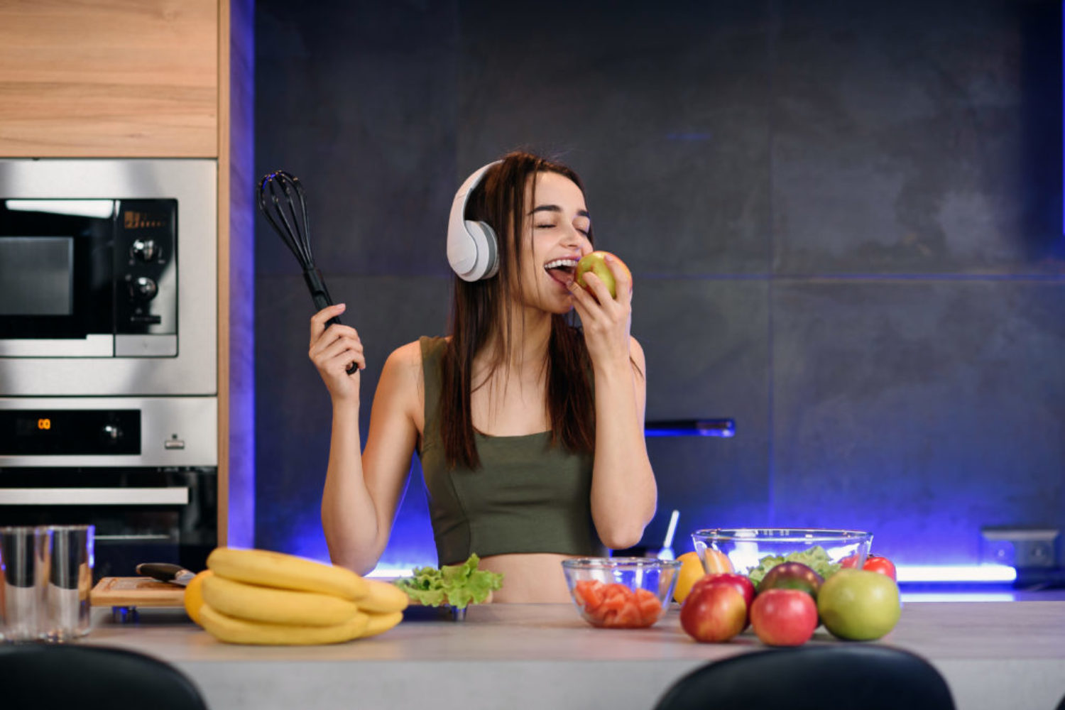 Young attractive woman eats red apple and listens to the music at kitchen in morning. Healthy lifestyle concept, enjoying breakfast.